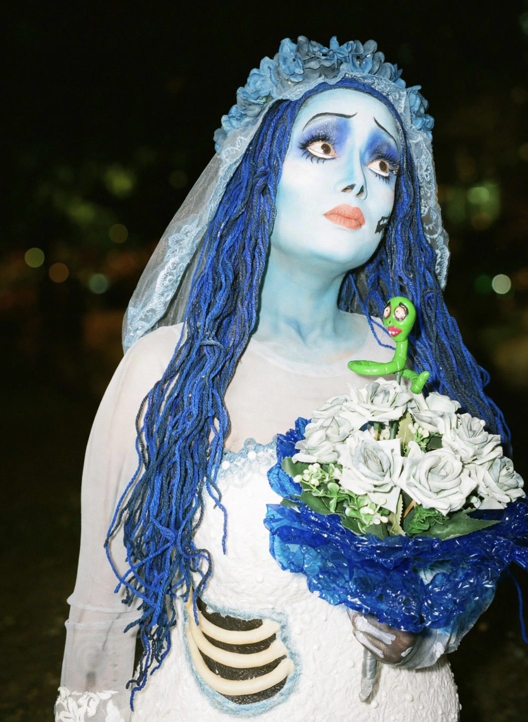 Noiva do Outro Mundo ao ar livre à noite, com a minhoquinha verde no ombro