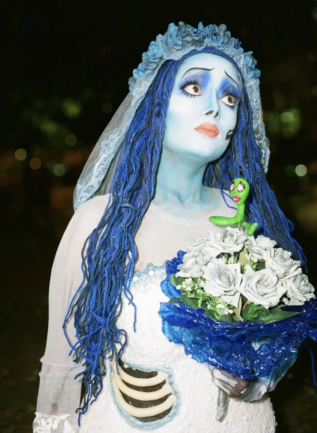 Noiva do Outro Mundo ao ar livre à noite, com a minhoquinha verde no ombro
