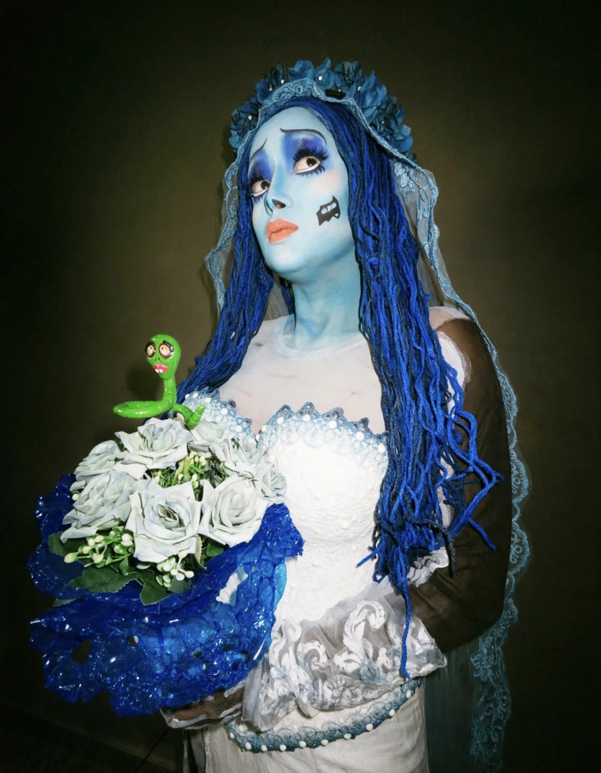 Noiva do Outro Mundo de pele azul e véu, segurando um buquê de rosas brancas