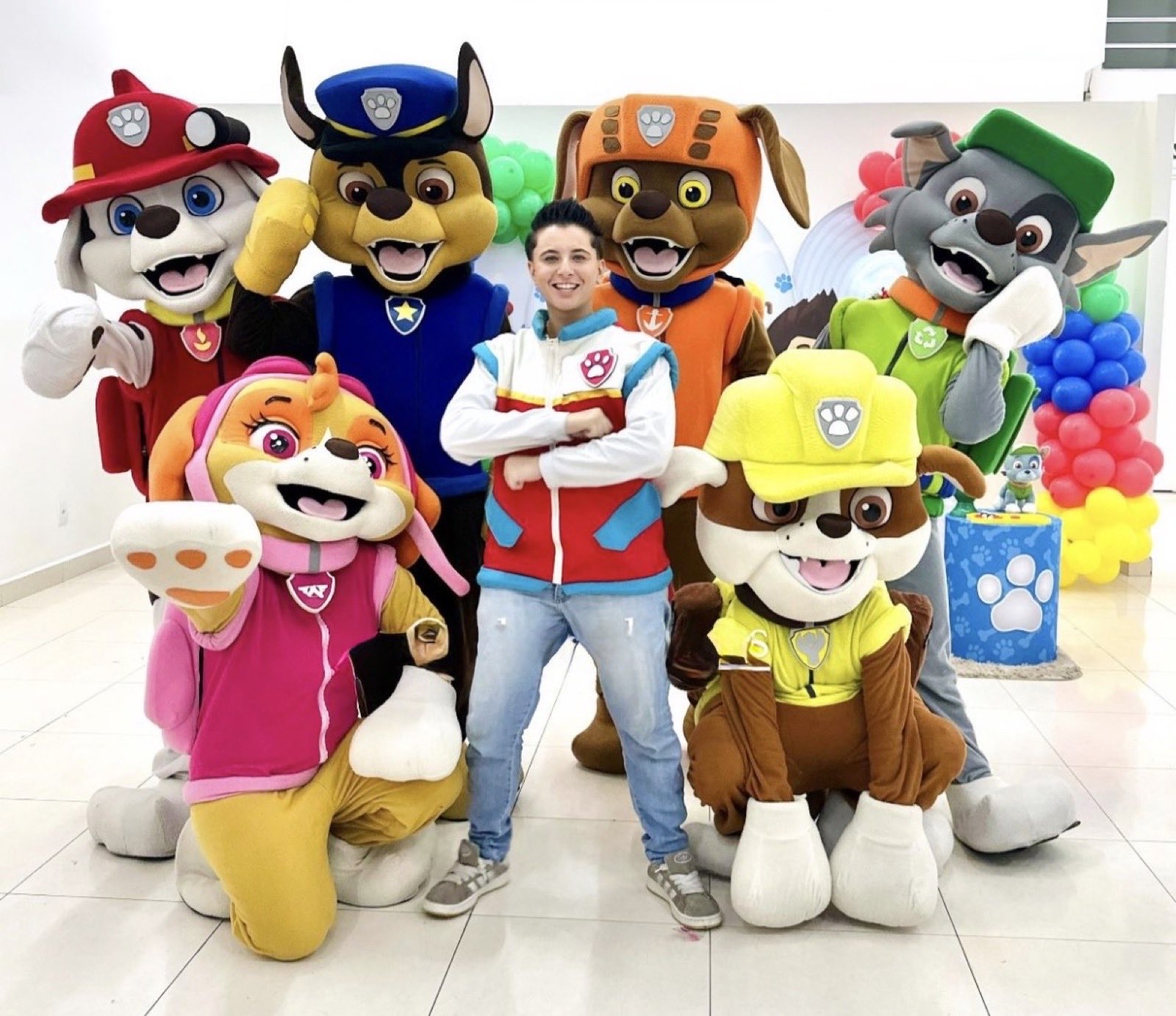 Seis mascotes filhotes de capacete colorido posando com o menino da patrulha numa festa