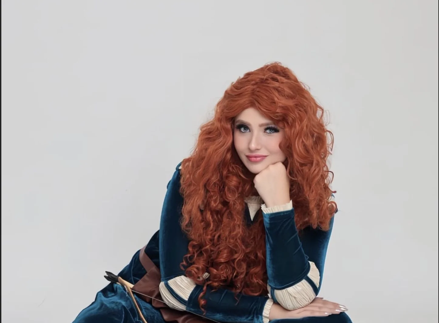 Arqueira Valente de cabelo ruivo cacheado e vestido azul-petróleo, com o arco ao lado