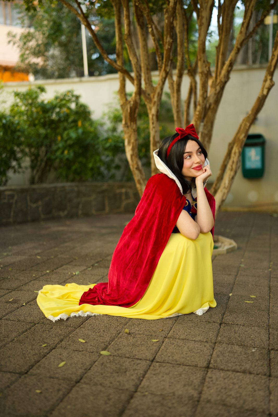 Princesa da Neve sentada no jardim com a capa vermelha estendida, olhando ao longe